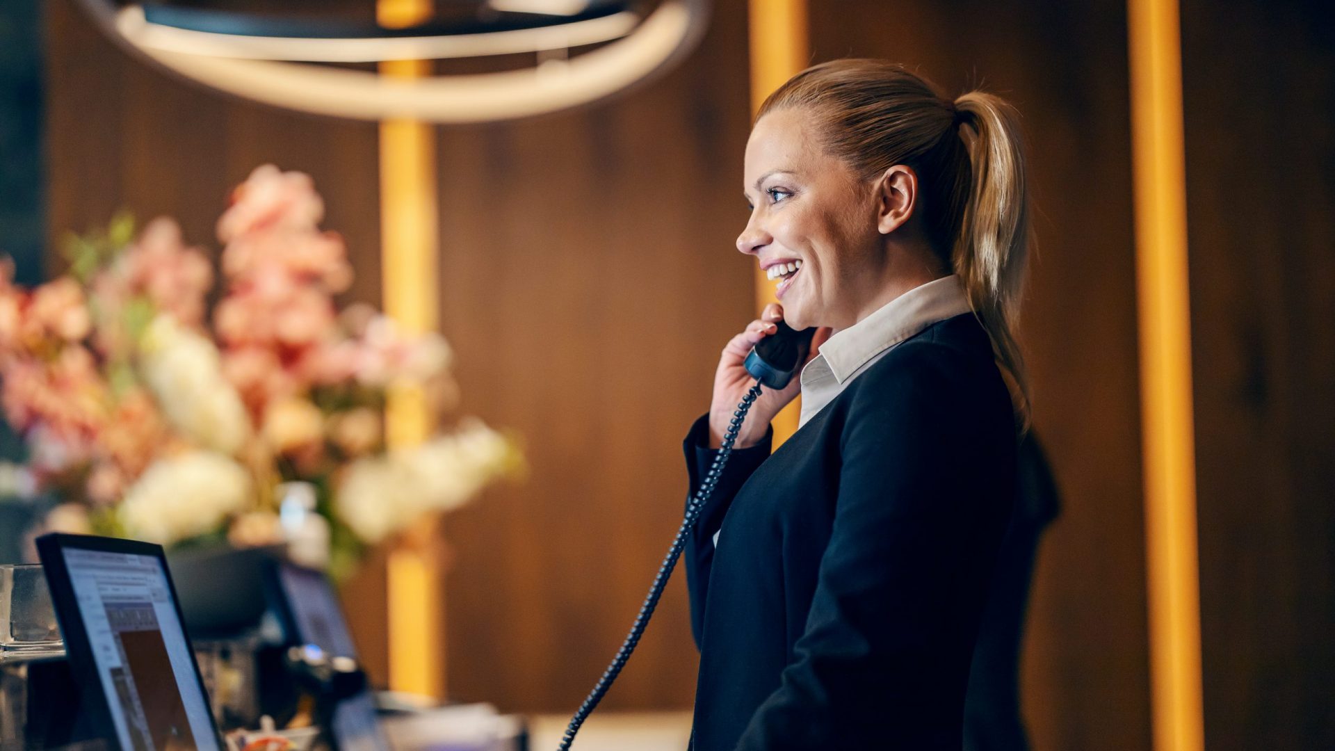 Profile of a happy receptionist answering calls at hotel reception.